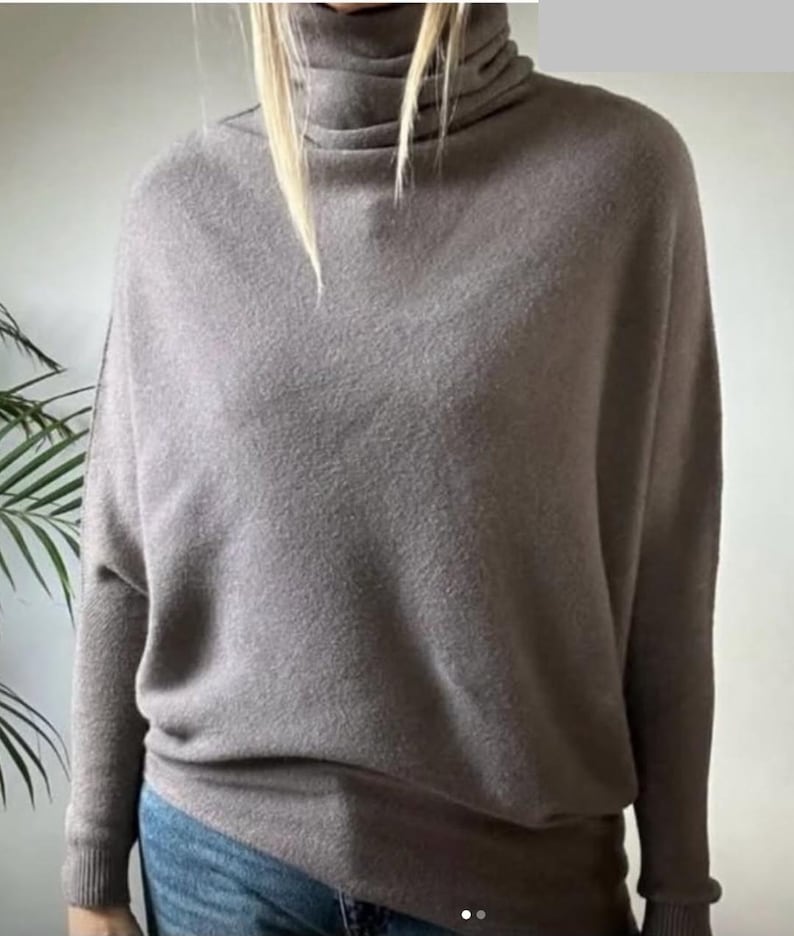Pu&ograve; includere: Un maglione dolcevita color talpa con maniche lunghe. Il maglione ha una vestibilit&agrave; ampia e orli e polsini a coste. La modella indossa jeans blu. Il maglione &egrave; realizzato in un materiale morbido, possibilmente a maglia.