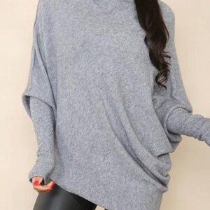 May include: A gray, long-sleeved, oversized sweater with a cowl neck and thumbholes.