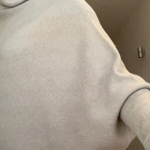 Pu&ograve; includere: Un maglione a collo alto grigio chiaro con una vestibilit&agrave; ampia. Il maglione ha maniche lunghe e un aspetto morbido e strutturato. Lo scollo &egrave; uno stile a collo alto ampio e drappeggiato.