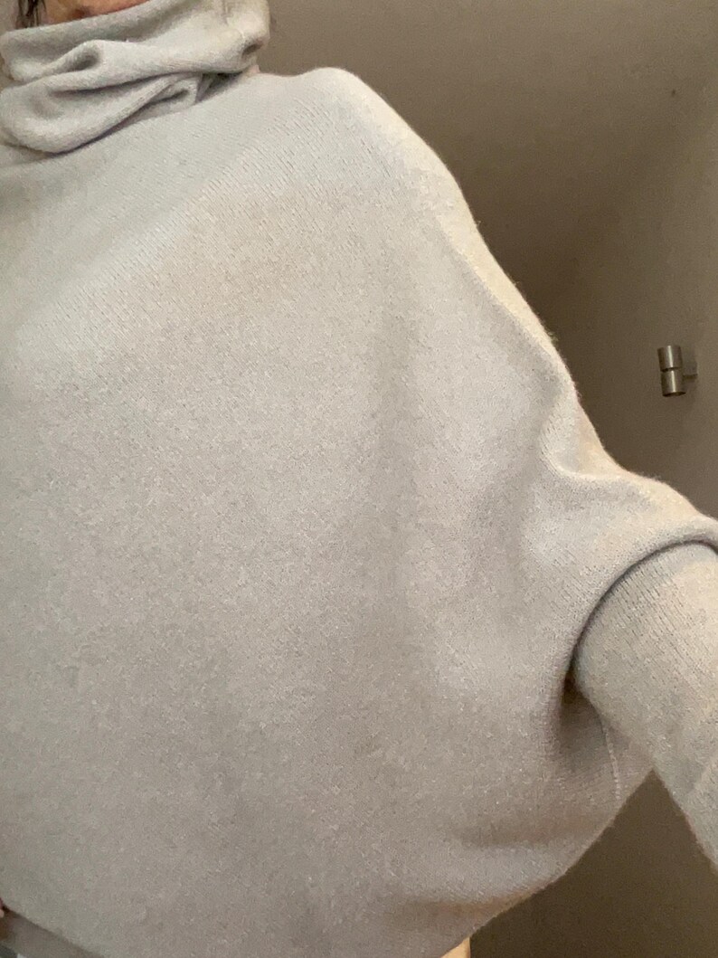 Pu&ograve; includere: Un maglione a collo alto grigio chiaro con una vestibilit&agrave; ampia. Il maglione ha maniche lunghe e un aspetto morbido e strutturato. Lo scollo &egrave; uno stile a collo alto ampio e drappeggiato.
