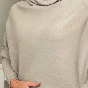 Pu&ograve; includere: Un maglione a collo alto beige chiaro con maniche lunghe. Il maglione ha una vestibilit&agrave; ampia e confortevole e un collo alto drappeggiato. Il tessuto appare morbido e caldo, adatto ai climi pi&ugrave; freschi. Le maniche sono lunghe e terminano ai polsi.