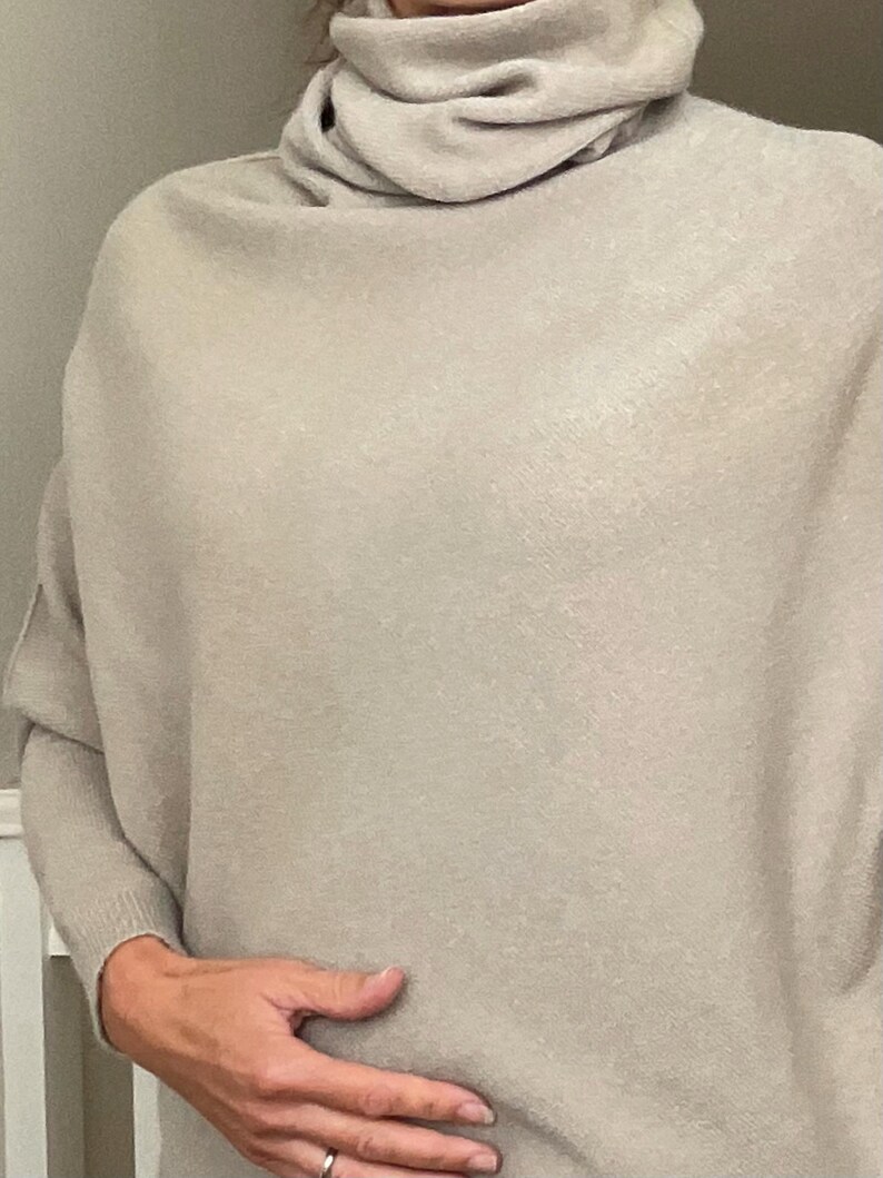 Pu&ograve; includere: Un maglione a collo alto beige chiaro con maniche lunghe. Il maglione ha una vestibilit&agrave; ampia e confortevole e un collo alto drappeggiato. Il tessuto appare morbido e caldo, adatto ai climi pi&ugrave; freschi. Le maniche sono lunghe e terminano ai polsi.