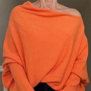May include: A bright orange, oversized sweater with a draped neckline and long sleeves.