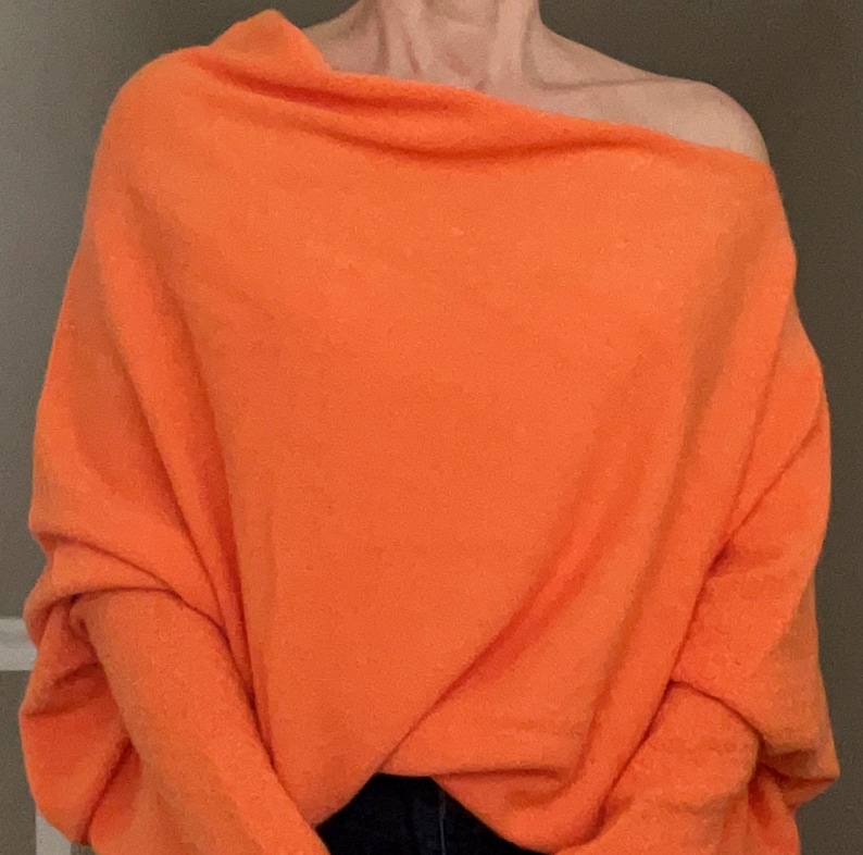 May include: A bright orange, oversized sweater with a draped neckline and long sleeves.