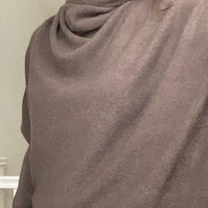 Pu&ograve; includere: Un maglione marrone con collo a cappuccio. Il maglione ha uno scollo drappeggiato e maniche lunghe. Il tessuto appare morbido e ha una lucentezza sottile. Lo stile generale &egrave; casual e confortevole, adatto ai climi pi&ugrave; freschi.