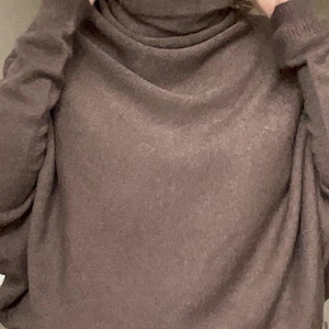 Pu&ograve; includere: Un maglione marrone a collo alto con maniche lunghe. Il maglione ha una vestibilit&agrave; ampia e confortevole e un collo alto e ripiegato. Il tessuto sembra morbido e strutturato.