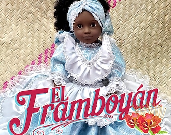 Puede incluir: Una muñeca de piel oscura, vestida con un vestido azul claro con adornos de encaje blanco y un pañuelo a juego. La muñeca tiene cabello negro rizado y está etiquetada como "-YEMAYA-" y "EL Framboyán" en la imagen.