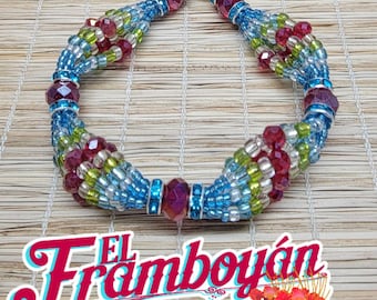 Può includere: Una collana di perline dal design vivace. La collana presenta perline blu, verdi e rosse, con perline sfaccettate più grandi in viola. Il testo "El Framboyán" è visualizzato in un carattere corsivo.