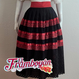 May include: A black skirt with red lace and ribbon accents, featuring a wide red waistband. The skirt has a scalloped hem and is displayed on a mannequin. The text "El Framboyán" is visible on the skirt.