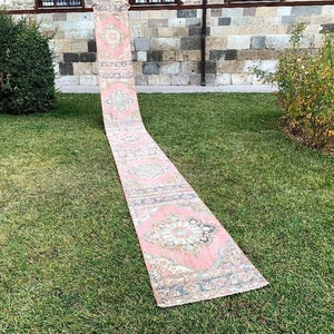 May include: A long, pink and blue patterned rug with intricate designs. The rug is laid out on a grassy lawn.