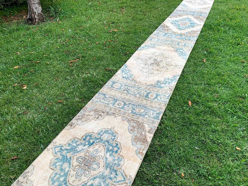 May include: A long, cream-colored rug with a blue and brown geometric pattern. The rug is laid out on a grassy lawn.
