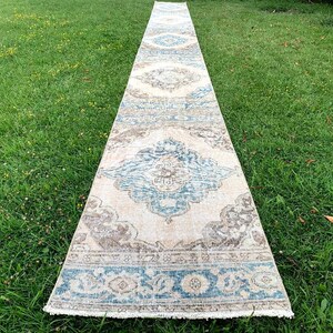 May include: A long, rectangular rug with a cream background and a blue and brown patterned design. The rug has a fringe border.