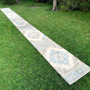 May include: A long, white runner rug with a blue and gray floral pattern. The rug is laid out on a green grassy lawn.