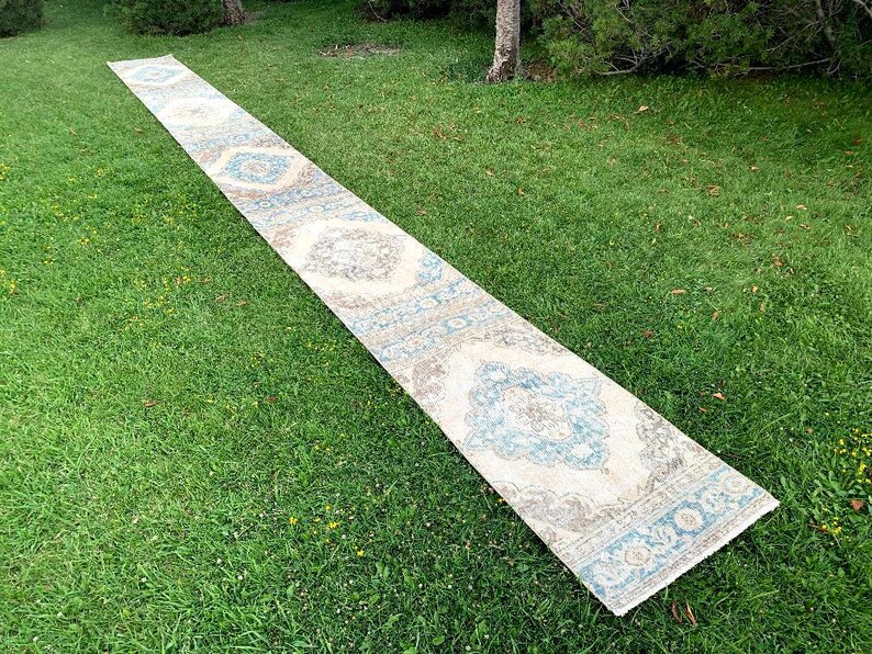 May include: A long, white runner rug with a blue and gray floral pattern. The rug is laid out on a green grassy lawn.