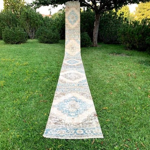 May include: A long, rectangular rug with a white background and a blue and brown geometric pattern. The rug is laid out on a green lawn.
