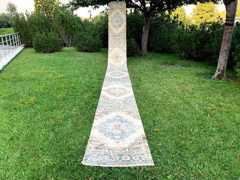 May include: A long, rectangular rug with a white background and a blue and brown geometric pattern. The rug is laid out on a green lawn.