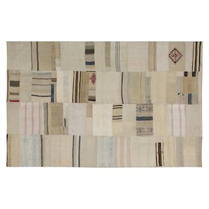 Puede incluir: Una alfombra rectangular de patchwork en tonos neutros. La alfombra está compuesta por varias piezas rectangulares en tonos beige, crema y marrón, con sutiles rayas y patrones geométricos en marrón, azul y rojo. La alfombra tiene una estética vintage y artesanal.