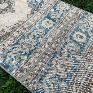 May include: A vintage rug with a light beige background and a blue and brown geometric pattern. The rug has a distressed look and is perfect for adding a touch of bohemian style to any room.