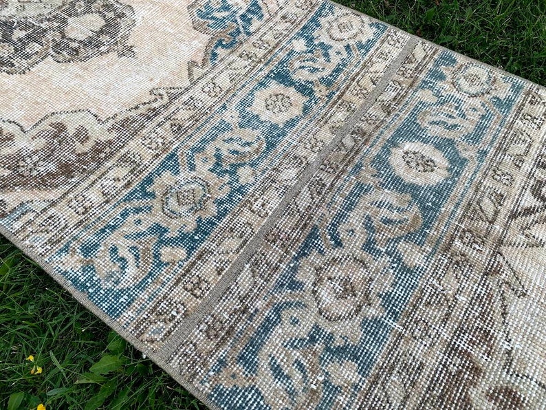 May include: A vintage rug with a light beige background and a blue and brown geometric pattern. The rug has a distressed look and is perfect for adding a touch of bohemian style to any room.