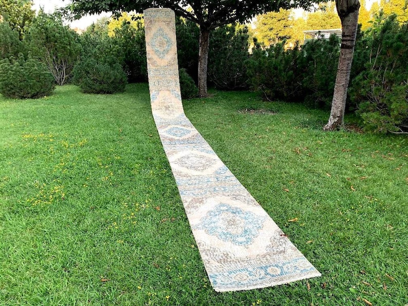 May include: A long, white runner rug with a blue and gray geometric pattern. The rug is laid out on a green lawn.