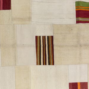 Puede incluir: Una alfombra patchwork con una paleta de colores neutros. La alfombra está compuesta por parches rectangulares y cuadrados en blanco roto, beige y crema. Acentos de rayas rojas, verdes y naranjas añaden toques de color. La alfombra tiene una estética vintage y artesanal.