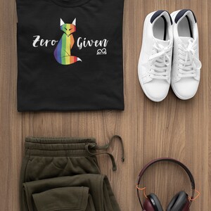 May include: A black t-shirt with a rainbow fox graphic and the text "Zero Given". The shirt is paired with olive green sweatpants, white sneakers, and burgundy headphones.
