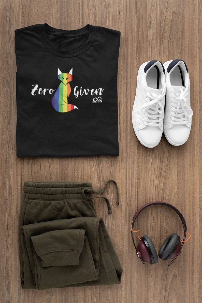 May include: A black t-shirt with a rainbow fox graphic and the text "Zero Given". The shirt is paired with olive green sweatpants, white sneakers, and burgundy headphones.