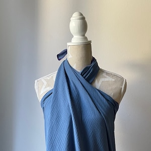 Può includere: Un top a portafoglio color blu polvere realizzato in tessuto testurizzato e stropicciato. Il capo presenta uno scollo all'americana con fasce di tessuto che si incrociano sul petto e si annodano dietro il collo, creando un aspetto drappeggiato.