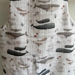 K&ouml;nnte beinhalten: Ein wei&szlig;er Stoff mit einem sich wiederholenden Muster aus Walen, Narwalen und Wasserpflanzen in Grau-, Braun- und Rott&ouml;nen. Der Stoff hat ein strukturiertes, geknittertes Aussehen. Das Design zeigt Wale und Narwale in verschiedenen Gr&ouml;&szlig;en.