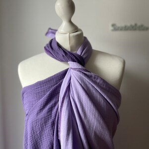 Può includere: Un involucro viola a due toni, drappeggiato su un manichino. L'involucro è una combinazione di tessuti viola chiaro e scuro, con un nodo sulla spalla. Il tessuto appare morbido e strutturato, adatto a una sciarpa o uno scialle.