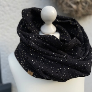 May include: Black infinity scarf with gold metallic flecks. The scarf is made of soft fabric and is draped over a white mannequin head. A small brown tag is visible on the scarf.