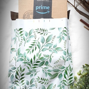 May include: White mailing envelope with a green leafy pattern. The envelope has a brown package on top with the Amazon Prime logo.
