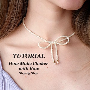 Op de afbeelding: Een witte kralen choker met een strik aan de voorkant. De ketting wordt gedragen door een persoon met een lichte huid en bruin haar. De tekst "TUTORIAL How Make Choker with Bow Step by Step" staat onder de ketting.