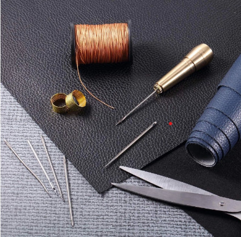 May include: A set of leatherworking tools including a spool of copper thread, two thimbles, a leather awl, four needles, and a pair of scissors.
