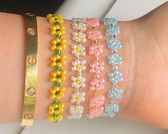 Puede incluir: Cinco pulseras de cuentas con diseños de flores. Las pulseras son de color amarillo, blanco, rosa y azul.