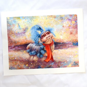 Puede incluir: Una pintura de acuarela de una criatura vermiforme azul y roja con una peluca azul y una bufanda roja. La criatura est&aacute; sentada sobre un fondo marr&oacute;n y amarillo con salpicaduras de pintura blanca y azul.