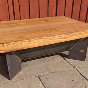 May include: A wooden coffee table with a natural wood finish and a metal frame. The table has a rectangular top and four legs. The legs are made of metal and have a black finish.