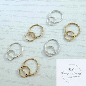 May include: Five pairs of interlocking rings, two gold and three silver, with a textured finish. The rings are arranged on a light wood surface. The image includes the text "Forever Linked Permanent Jewelry Supplies".