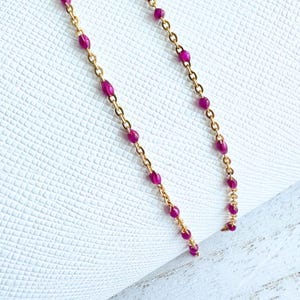May include: A gold chain necklace with small, round, pink beads.