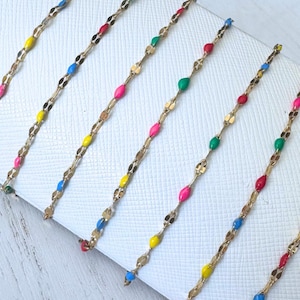 May include: Six gold chains with colorful enamel beads. The chains are arranged in a row on a white surface. The beads are in the colors red, blue, green, yellow, and pink.