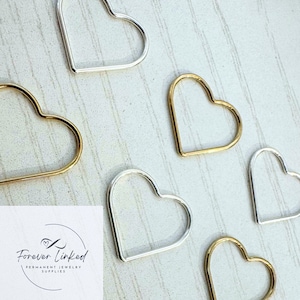 May include: Five heart-shaped hoops, two gold and three silver, on a white wooden surface. The hoops are all the same size and shape, and they are arranged in a random pattern. The text "Forever Linked" is visible in the lower left corner of the image.