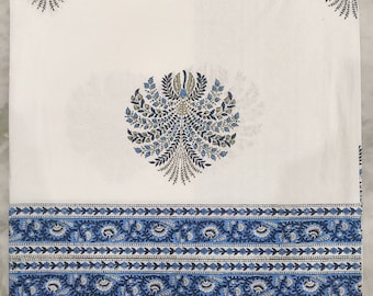 Op de afbeelding: Wit katoenen beddengoed met een blauwe en groene bloemenprint. Het laken heeft een rand met een herhalend patroon van blauwe bloemen en bladeren.