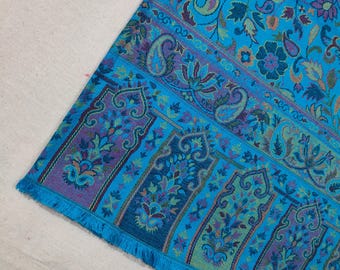 May include: A blue paisley patterned shawl with a fringed edge. The shawl has a repeating pattern of floral and paisley designs in shades of blue, green, purple, and pink.