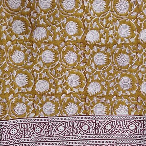 May include: A mustard yellow fabric with a white floral pattern and a maroon border. The border has a repeating pattern of white flowers and leaves.