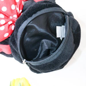 May include: Black plush bag with a zippered opening. A large red bow with white polka dots is attached to the top. The bag has a black interior and a small tag inside. Yellow tulips are in the bottom corner.