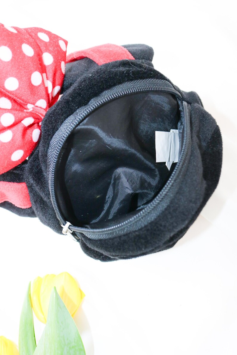 May include: Black plush bag with a zippered opening. A large red bow with white polka dots is attached to the top. The bag has a black interior and a small tag inside. Yellow tulips are in the bottom corner.