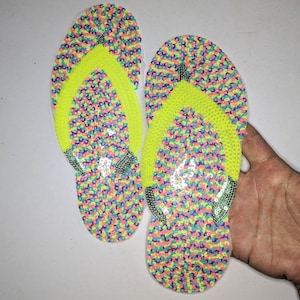 May include: A pair of colorful flip-flop shaped patches with a neon yellow strap. The patches are made of sequins and are perfect for adding a fun and festive touch to any project.