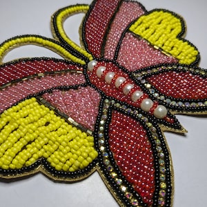 May include: A beaded butterfly applique with red, pink, yellow, and black beads. The butterfly has a row of white pearl beads down the center.