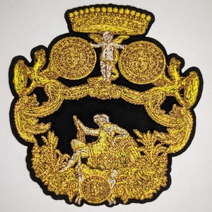 May include: A gold embroidered patch with a black background featuring a crown, a cherub, and a woman sitting on a throne. The patch is surrounded by ornate scrollwork and floral designs.
