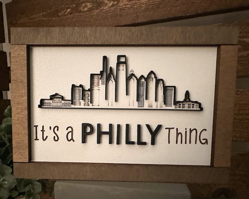 Puede incluir: Un letrero de madera con una silueta negra del horizonte de Filadelfia y el texto "It's a Philly Thing".